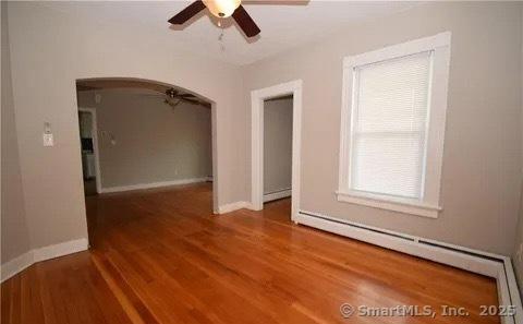 empty room with hardwood / wood-style floors, baseboard heating, and ceiling fan