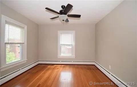 unfurnished room featuring baseboard heating, ceiling fan, and hardwood / wood-style floors