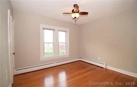 unfurnished room featuring wood-type flooring, ceiling fan, and a baseboard heating unit