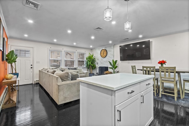 kitchen with a large fireplace, a kitchen island, dark hardwood / wood-style floors, white cabinetry, and hanging light fixtures