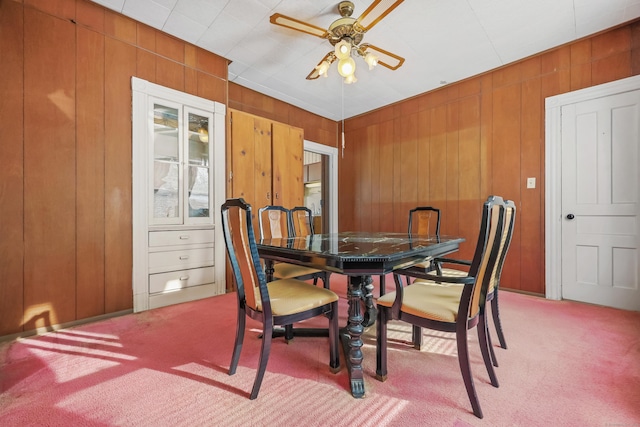 carpeted dining space featuring ceiling fan and wooden walls