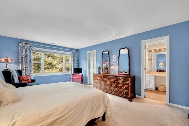 bedroom featuring ensuite bath, light colored carpet, and baseboards