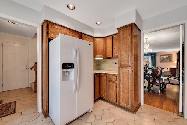 kitchen with a chandelier, light countertops, decorative backsplash, brown cabinets, and white fridge with ice dispenser