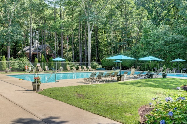 community pool with a patio area, a lawn, and fence