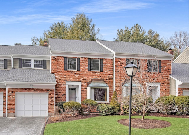 view of front of home with a front lawn, driveway, a shingled roof, a garage, and brick siding