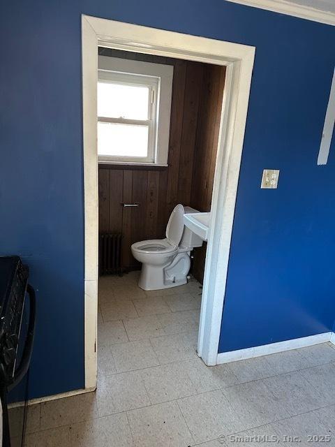 bathroom featuring toilet, radiator, ornamental molding, and wood walls