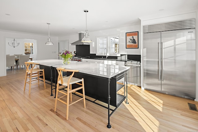 kitchen featuring a kitchen bar, wall chimney exhaust hood, stainless steel built in fridge, and a center island