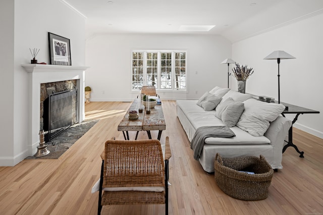 living room with light hardwood / wood-style floors, ornamental molding, and vaulted ceiling with skylight