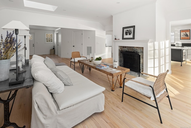 living room featuring a tile fireplace, light hardwood / wood-style floors, and lofted ceiling with skylight