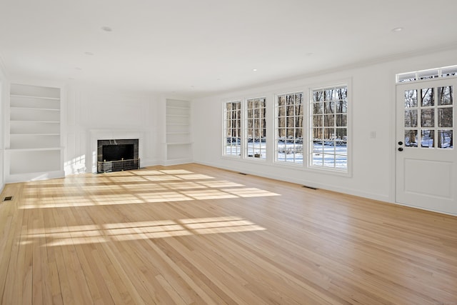 unfurnished living room featuring built in shelves, light hardwood / wood-style floors, and crown molding