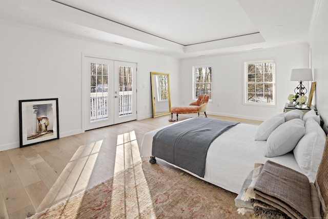 bedroom with a tray ceiling, french doors, light wood-type flooring, and access to outside