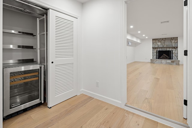 bar with light hardwood / wood-style flooring, a stone fireplace, and beverage cooler