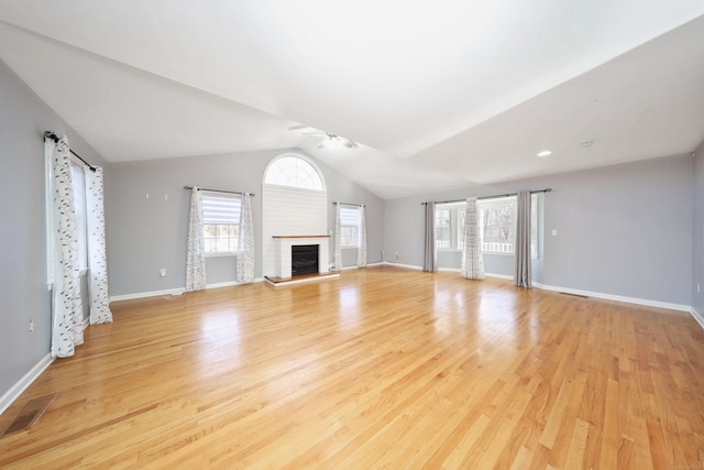 unfurnished living room featuring a fireplace, light hardwood / wood-style floors, a wealth of natural light, and lofted ceiling