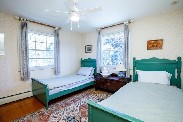 bedroom with multiple windows, hardwood / wood-style floors, a baseboard radiator, and ceiling fan