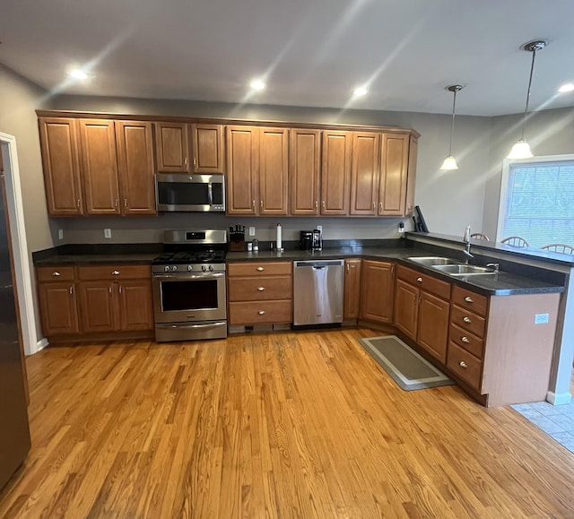 kitchen featuring sink, stainless steel appliances, hanging light fixtures, and light hardwood / wood-style flooring