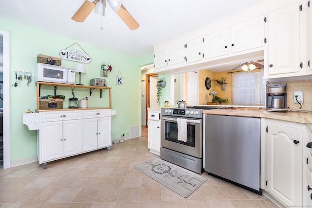 kitchen featuring ceiling fan, dishwasher, light tile patterned flooring, white cabinetry, and stainless steel range oven