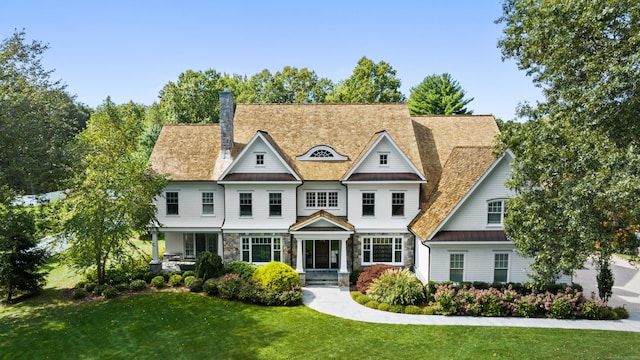 shingle-style home with metal roof, stone siding, a front lawn, a standing seam roof, and a chimney