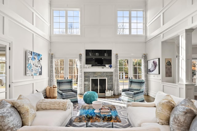 living area featuring a fireplace, a high ceiling, a decorative wall, and french doors