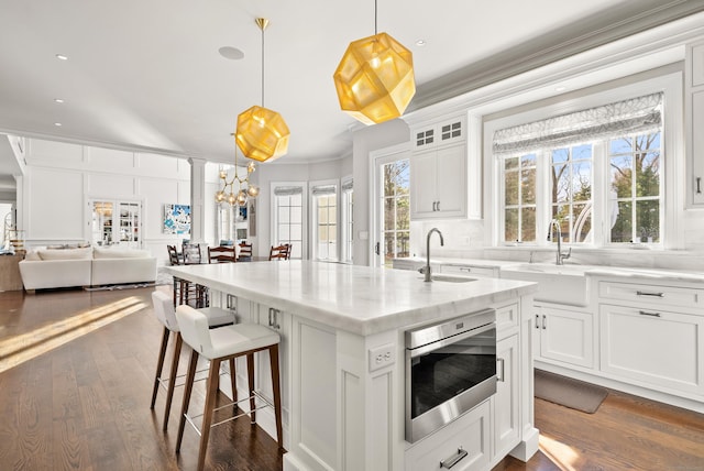 kitchen featuring a center island with sink, stainless steel microwave, open floor plan, white cabinetry, and pendant lighting