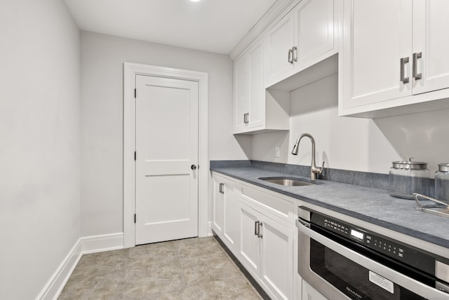 kitchen with dark countertops, baseboards, white cabinetry, and a sink