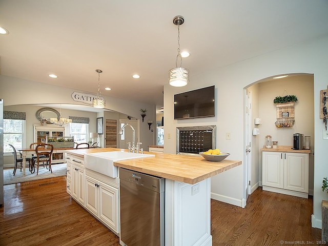 kitchen with wooden counters, stainless steel dishwasher, a kitchen island with sink, sink, and hanging light fixtures