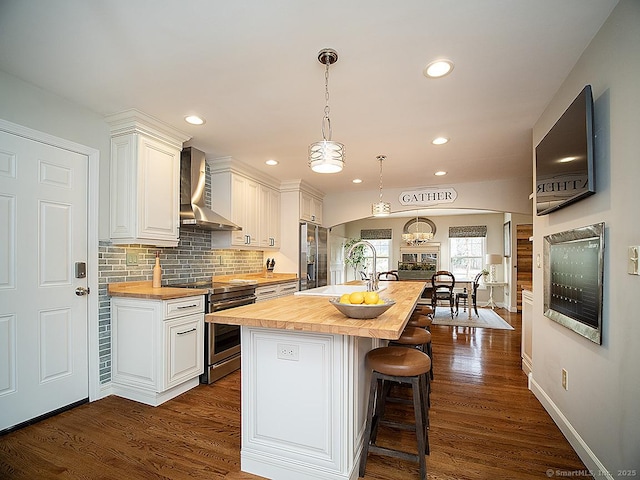 kitchen with butcher block counters, white cabinetry, stainless steel appliances, and wall chimney range hood