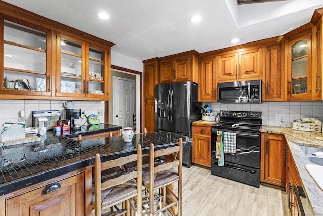 kitchen featuring light wood-type flooring, decorative backsplash, light stone counters, and black appliances