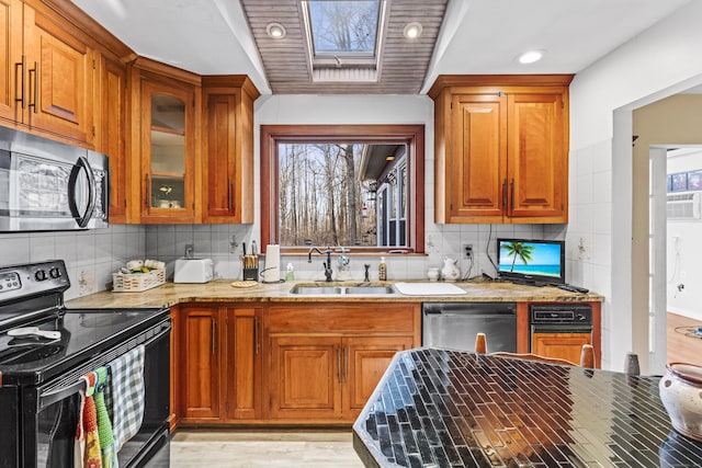 kitchen with light stone countertops, black appliances, a skylight, sink, and backsplash