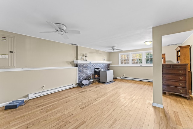 interior space with light hardwood / wood-style floors, a wood stove, a baseboard radiator, and ceiling fan