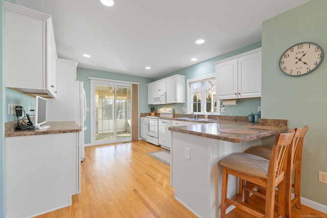 kitchen with kitchen peninsula, white appliances, white cabinets, light hardwood / wood-style floors, and a breakfast bar area