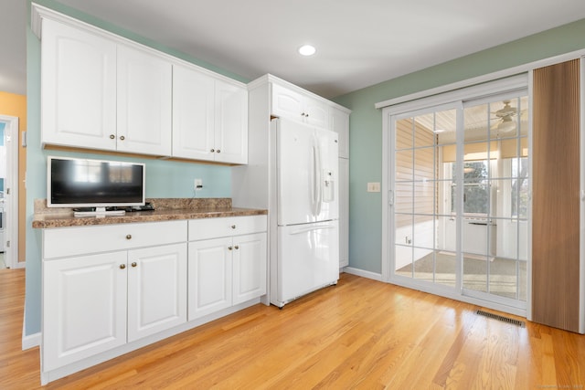 kitchen featuring light wood-type flooring, ceiling fan, white refrigerator with ice dispenser, dark stone countertops, and white cabinets