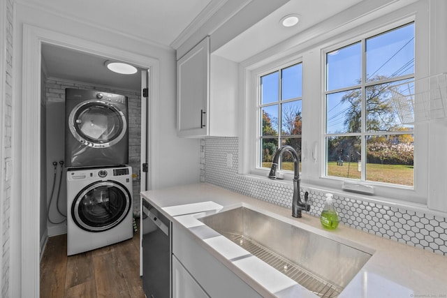 laundry room with sink, stacked washer and clothes dryer, a healthy amount of sunlight, and dark wood-type flooring