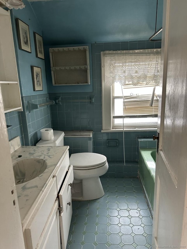 bathroom featuring a bathing tub, vanity, tile walls, and toilet