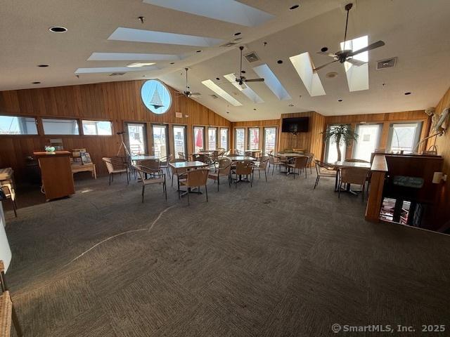 carpeted dining space featuring ceiling fan and vaulted ceiling with skylight