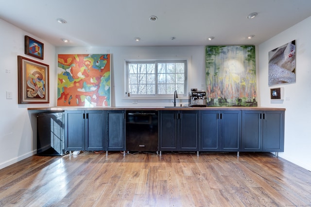 bar featuring black dishwasher, sink, and light hardwood / wood-style floors