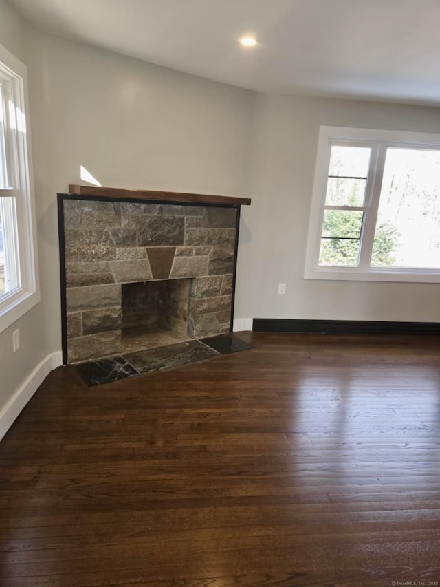 unfurnished living room featuring dark wood-type flooring, a healthy amount of sunlight, and a stone fireplace