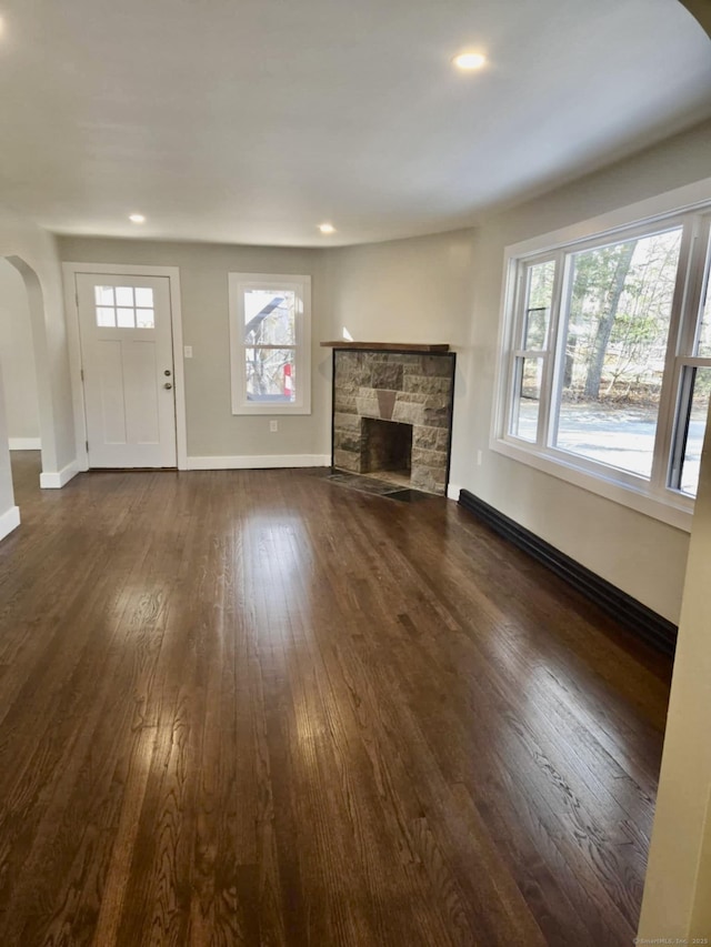 unfurnished living room with a baseboard radiator, dark hardwood / wood-style flooring, and a stone fireplace