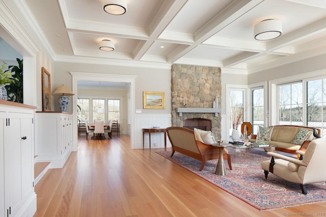 living area featuring a wealth of natural light, ornamental molding, coffered ceiling, beam ceiling, and a stone fireplace