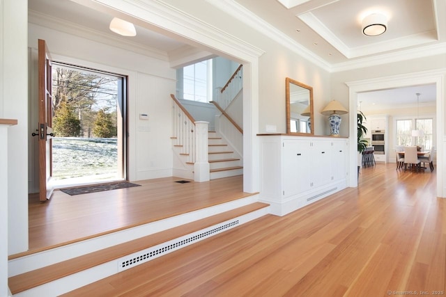 entryway with a tray ceiling, hardwood / wood-style floors, plenty of natural light, and ornamental molding