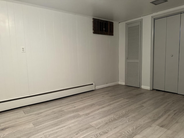 unfurnished bedroom featuring baseboard heating, two closets, and light wood-type flooring