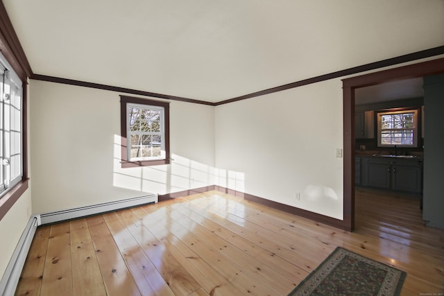 spare room featuring baseboard heating, sink, ornamental molding, and light hardwood / wood-style flooring