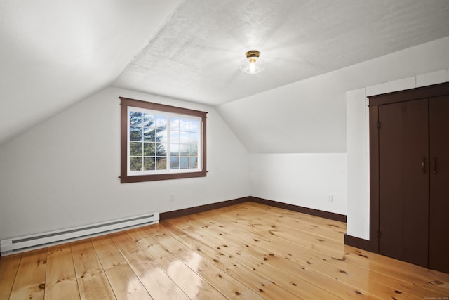 additional living space with baseboard heating, vaulted ceiling, and light wood-type flooring