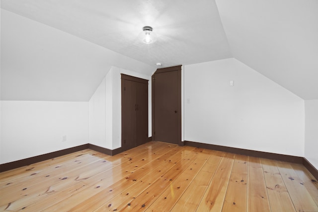 additional living space with light hardwood / wood-style floors and vaulted ceiling