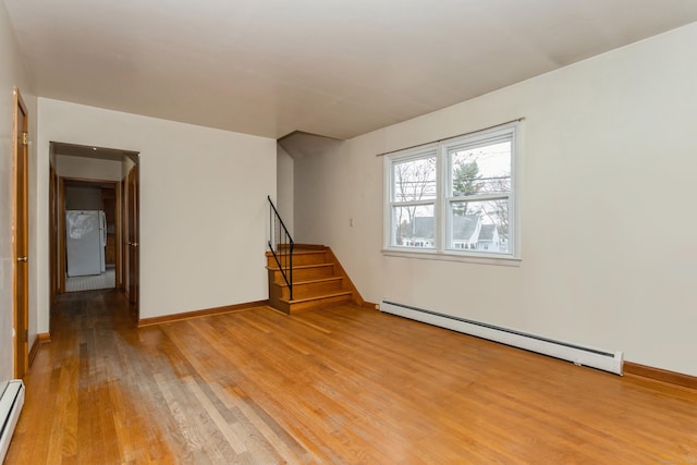 spare room featuring baseboard heating and light hardwood / wood-style flooring