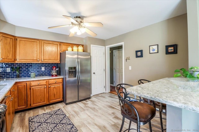 kitchen with stainless steel refrigerator with ice dispenser, ceiling fan, tasteful backsplash, light hardwood / wood-style floors, and light stone counters