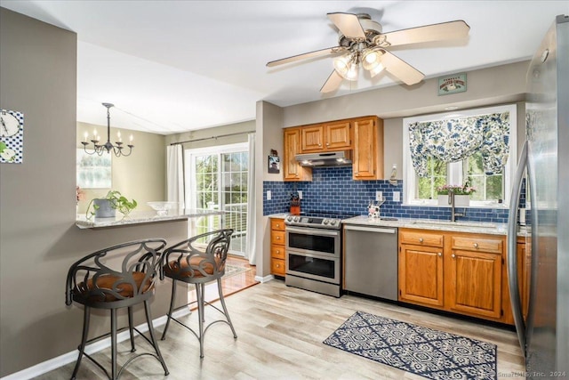 kitchen with ceiling fan with notable chandelier, a kitchen breakfast bar, sink, hanging light fixtures, and stainless steel appliances