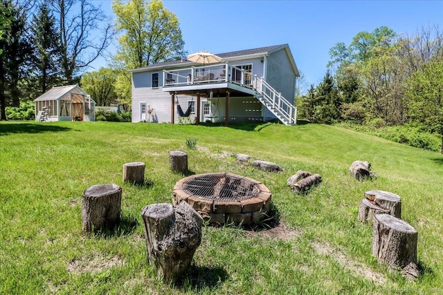 back of house featuring a lawn, an outbuilding, a deck, and an outdoor fire pit