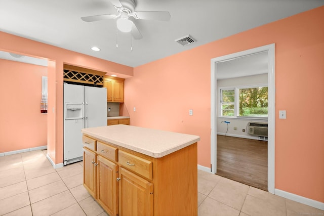 kitchen featuring a wall unit AC, ceiling fan, a center island, white fridge with ice dispenser, and light tile patterned flooring