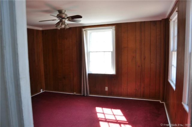 carpeted spare room with ceiling fan and wooden walls