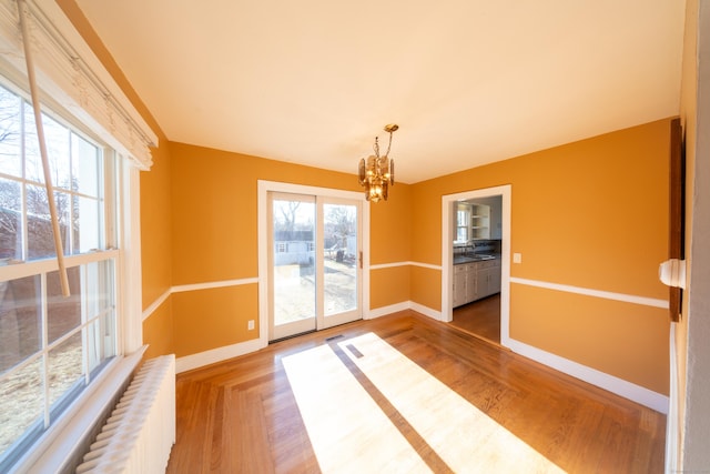 unfurnished dining area with hardwood / wood-style floors, a notable chandelier, plenty of natural light, and radiator